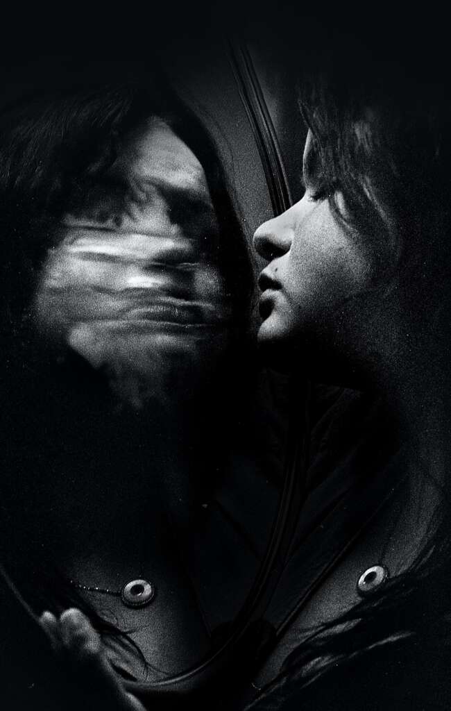 Woman with eyes closed with blurred reflection in mirror.